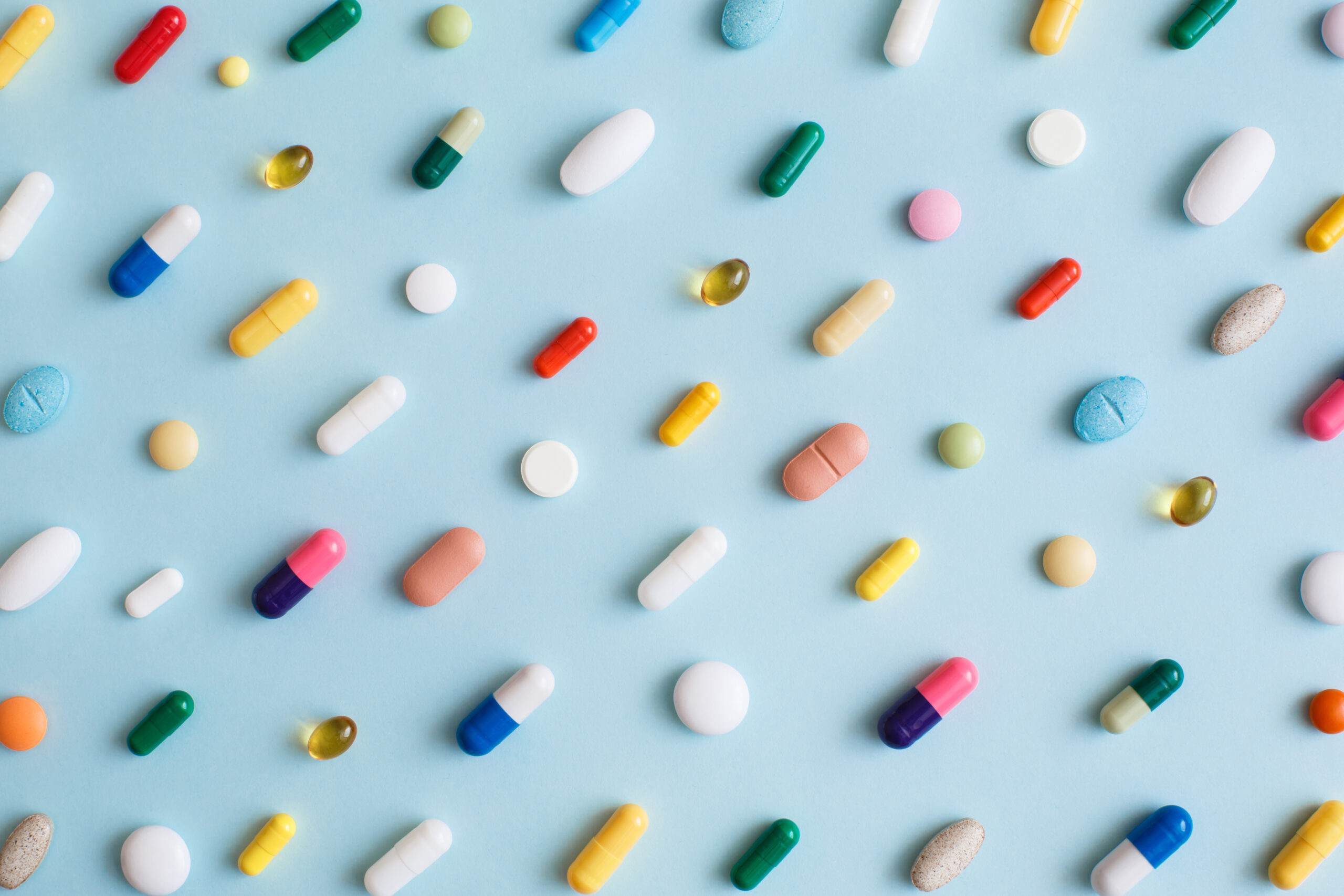 Creative layout of colorful pills and capsules on blue background. Minimal medical concept. Pharmaceutical, Covid-19 or Coronavirus. Flat lay, top view